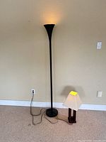Black torchiere floor lamp and wooden table lamp standing side by side, both illuminated