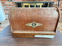 Wooden domed Singer carrying case front view highlighting veneer wear and logo medallion