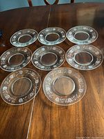 Eight clear etched floral glass plates displayed on wooden surface