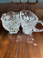 Clear pressed glass creamer and open sugar bowl with starburst diamond pattern on wooden table
