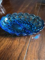 Angle showing full oval cobalt blue pressed glass dish with scalloped rim and starburst pattern