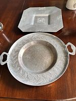 Round handled tray stacked atop octagonal tray showing leaf and floral motifs and overall wear