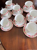Eight porcelain teacups each paired with matching saucer showing rose pattern and gold trim