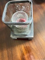 Square frosted glass votive holder on metal base with used pink candle visible