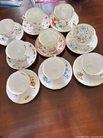 Nine teacup and saucer sets displayed on table, showing patterns and gold trim