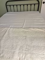 Full view of bed showing wrought iron headboard, mattress and bedding