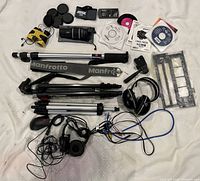 Overhead view of complete lot showing tripods, optics, headphones, caps, CDs, cables