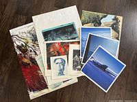Stack of assorted artworks on paper displayed on wood floor