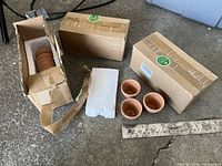 Open box showing stacked small terracotta pots, three loose for scale, ruler indicating size