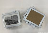 Two stacks of white 8x10 frames, one face-up showing printed insert, one face-down showing brown backs