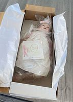 Doll wrapped in plastic lying in opened box with tissue paper