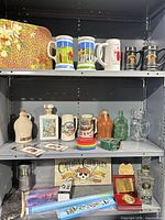 Shelves with steins, jugs, bottles, floral case and other items