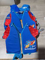 Stack showing two blue/red SwimSchool children’s vests atop blue adult life jacket