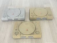 Three Sony PlayStation consoles on floor, showing overall condition