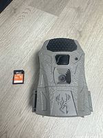 Front view of Wildgame Innovations grey trail camera alongside PNY 32 GB SD card