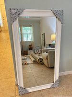 Full view of white framed wall mirror standing against wall with corner protectors