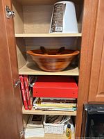 Cabinet shelves showing cookbooks, red binder, wooden bowl, baskets of recipes, lampshade
