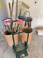 Overview of lot showing dolly, barrels filled with yard tools, barstool and fan