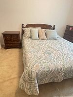 Queen bed with hardwood headboard, paisley bedding, nightstand at left
