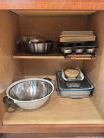 Overview of cabinet with mixing bowls, stacked bakeware, muffin tin, cutting board