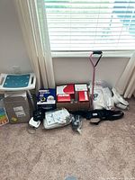 Overall lot against wall showing bath bench seat, boxes, cane, BP monitor, gait belt