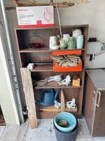 Full view of bookcase with contents including pottery, driftwood, watering can, planters