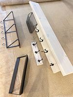 All shelving pieces laid out: large white shelf, wire basket, small hook rack, brown shelf with hooks, black frame shelf