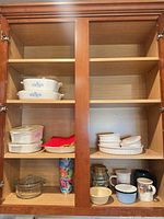 Full view of cabinet showing all Corning Ware dishes, white fluted dishes, Anchor Hocking casserole, mugs, bowls, jar and tumbler