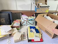 Overview of mixed stationery items on table including file holder, boxes, notebooks, pads