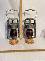 Front view of both Dietz lanterns showing red globes, cages, copper bases, ruler for scale