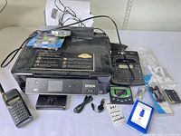 Lot overview showing Epson XP-410 printer with accessories, label maker, scanner and cables