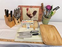 Lot overview showing knives in blocks, cutting boards, utensil holder with utensils and boxed Chef's Choice kit