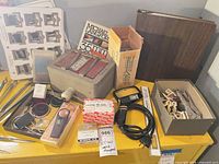 Overview of lot on yellow surface showing filter box, light meter, slide trays, power cord, loupe, tools, slide mounts and book