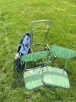 Two green/teal folding stadium seats, folding cart, blue carrying bag on grass