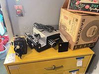 Projector body, transformer, power cord and box on yellow cabinet