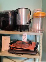 Shelf view showing black air fryer, stainless urn, clear container, white coffee maker part and orange electric grill with accessories