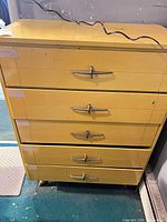 Front view of yellow five-drawer dresser with metal airplane-style handles