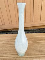Full side view of tall white swirled glass vase on wooden surface