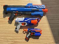 Overall view of all three foam-dart blasters laid out on wood surface