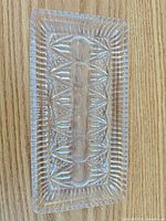 Top view of clear pressed glass tray showing starburst/geometric patterns and sawtooth rim