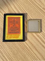 Framed Yant textile beside empty gilt frame on wood surface