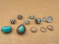 11 rings arranged on cardboard, showing variety of stones and metal tones