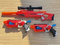 Full view of Alpha Rogue rifle with scope and two X-Shot pistols