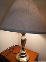 Full view of brass lamp with shade on wooden surface