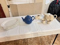 All items on table: blue teapot, camel teapot, camel creamer, two cups, stack of four plates