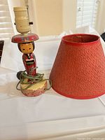 Kokeshi doll lamp base, socket, red shade, cord visible