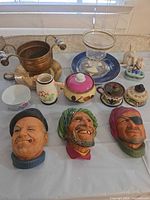 Group shot of copper bowl, glass cup, rabbit figurine, blue plate, ceramics and three ceramic head plaques