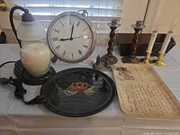 Lot overview showing Couroc tray, wax warmer lamp, clock, wooden and brass candlesticks, postcard plaque and NYC miniature