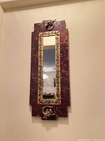 Full view of rectangular burgundy and gold framed mirror mounted on wall