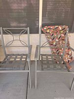 Two gray metal patio chairs side by side with patterned cushion leaning